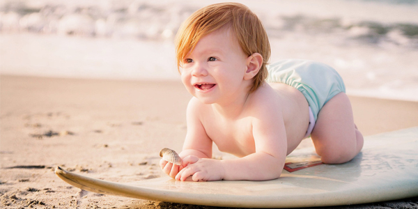 Kleinkind am Strand auf Surfbrett mit Muschel